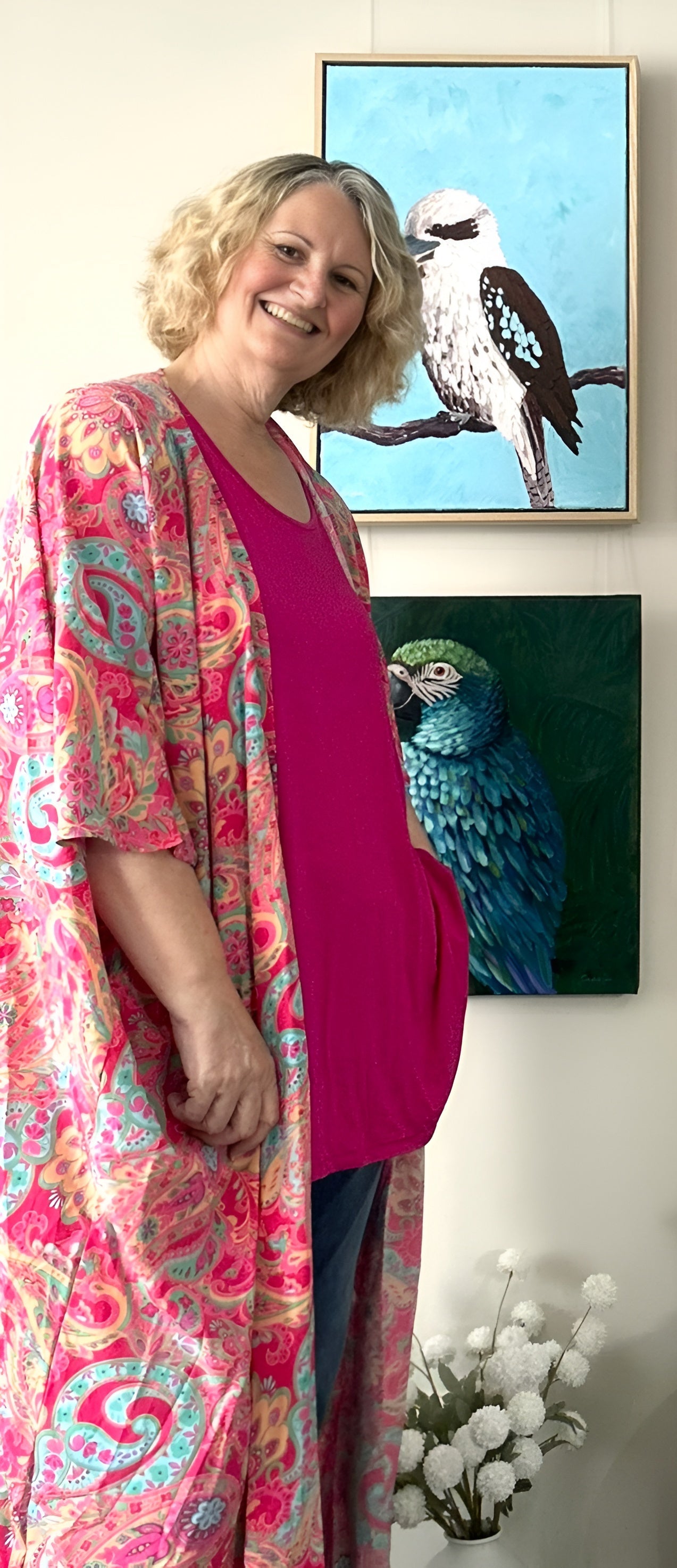Artist Cassie Holmes standing in a room with colourful bird-themed wall art
